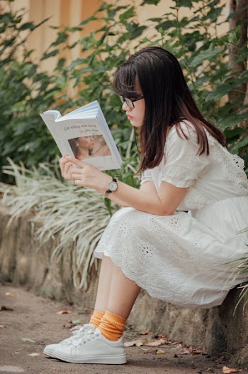 Woman Sitting on Gray Concrete Block Reading Book