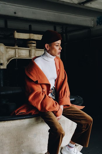 Woman Sitting on Gray Surface Wearing Orange Topcoat