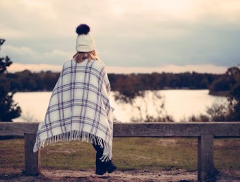 woman sitting on gray wooden bench viewing body of water