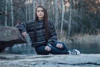 woman sitting on pavement hands against stone near body of water