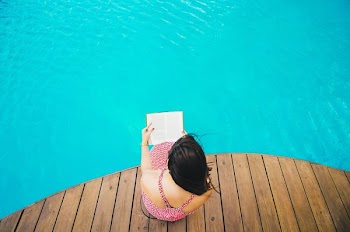 woman sitting on poolside dock while riding book