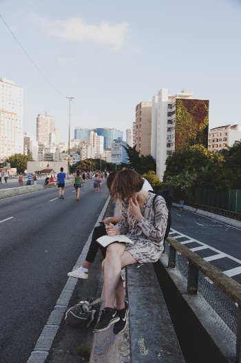 Woman Sitting on Railings Under Grey Clouds