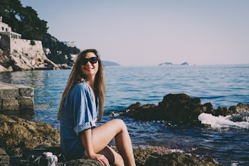 Woman Sitting on Rock Formation on Shoreline