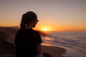 woman sitting on sand during sunset