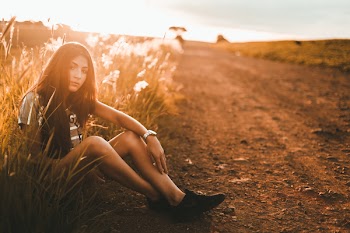 Woman Sitting on Sand Surrouded by Kans Grass during Sunset
