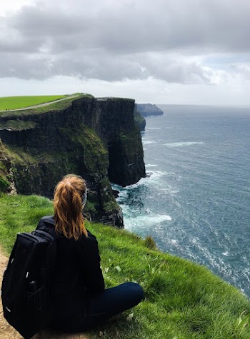 Woman Sitting on Sea Cliff Under Cloudy Sky