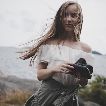 Woman Sitting on Seashore Holding Camera