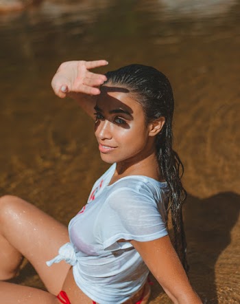Woman Sitting on Shore While Raising Her Right Hand