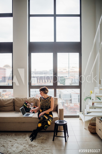 Woman sitting on sofa and drinking wine during video call