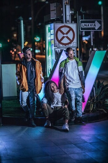 Woman Sitting on Street Curb in Between Two Men Standing in Front of Road Sign