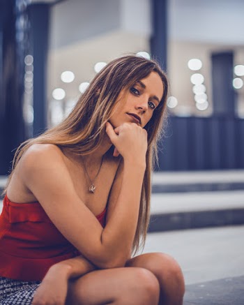Woman Sitting on Surface With Hand on Chin