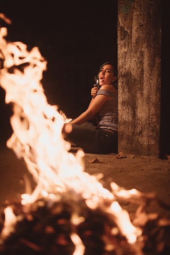 Woman Sitting on the Ground Beside Pillar Sticking Her Tongue Out Near Bonfire