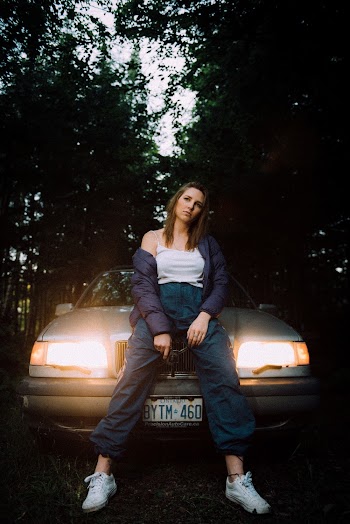 Woman Sitting on Vehicle Hood With Lighted Headlights Near Trees