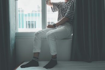 Woman Sitting on Window Stepping on White Bed Inside Well Lighted Room