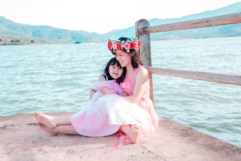 Woman Sitting While Holding Girl Near Body Of Water
