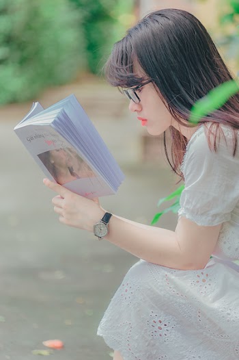 Woman Sitting While Reading Book Outdoors