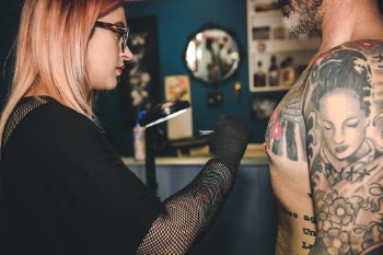 Woman sketching a tattoo drawing on a man's chest