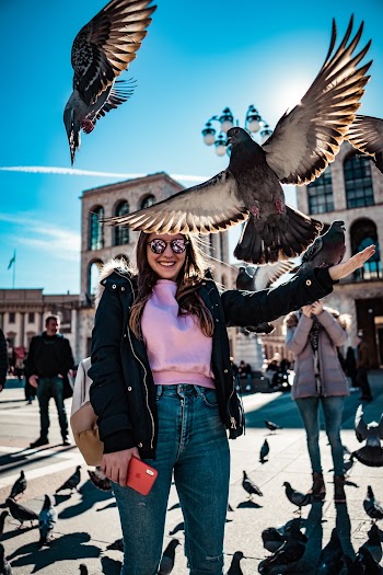 Woman Smiles and Stands Near Flying Pigeons
