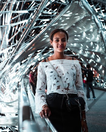 Woman Smiling and Standing While Holding on Gray Stainless Steel Railings Surrounded With People