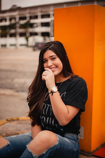 Woman Smiling Wearing Black Shirt Sitting Beside Orange Painted Post