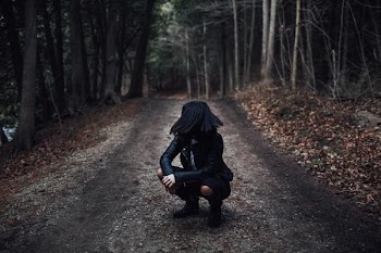 woman squatting on gray dirt road surrounded by trees