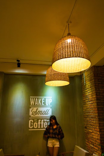 Woman Standing and Leaning Beside Wake Up Smell the Coffee Text Wall