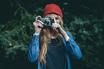 woman standing behind green leaf tree holding DSLR camera