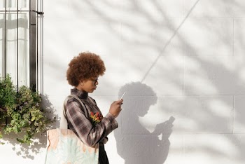 Woman Standing Beside A Wall Looking At Her Phone