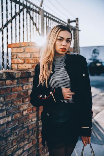 woman standing beside brown wall cladding holding her stomach