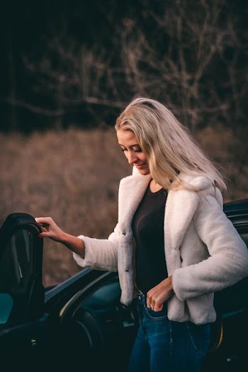 woman standing beside car near bare trees during golden hour