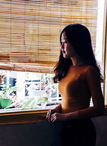 Woman Standing Beside Window Blinds and Plants