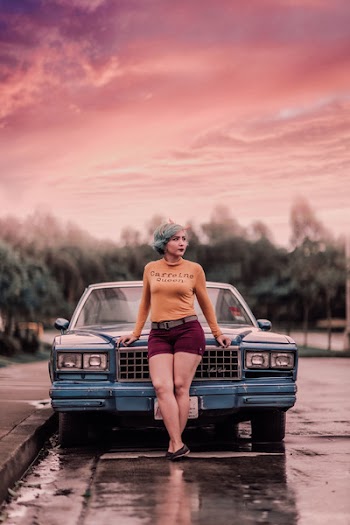 Woman Standing in Front of Blue Vehicle Under Cloudy Sky