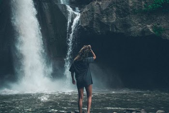 woman standing in front of waterfalls while holding her hair