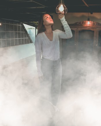 Woman Standing Inside Smoky Room and Holding Turned on Hanging Light Bulb