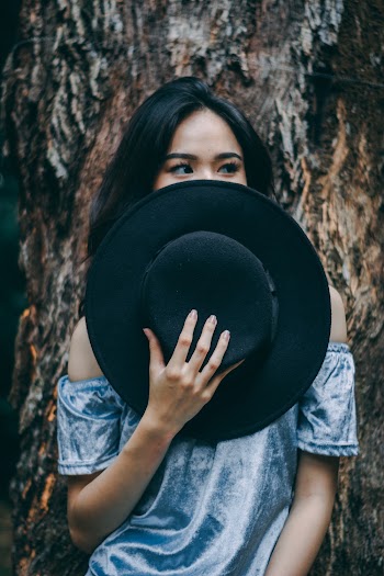 Woman Standing Near A Tree Holding A Black Hat