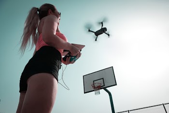 Woman Standing Near Basketball Hoop Controlling Drone