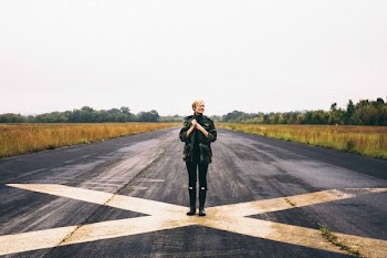 woman standing on black asphalt between green grass under clear blue sky during daytime