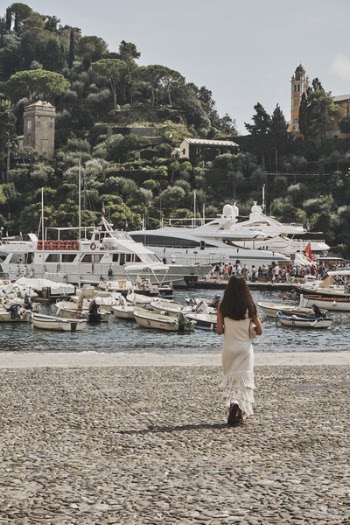 Woman Standing on Brown Ground Beside Body of Water With Assorted Boats and Yacht Under Blue Sky
