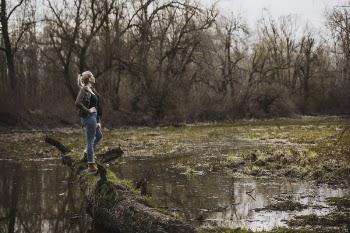 Woman Standing on Driftwood Above Body of Water