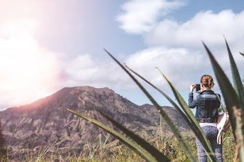 Woman Standing on Green Grass Field Taking Photo of Mountain
