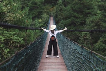 woman standing on hanging bridge surrounded by trees