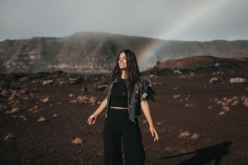 woman standing on mountain behind rainbow