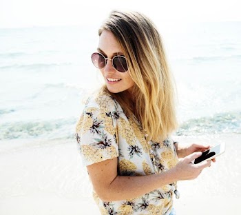 woman standing on shore holding smartphone