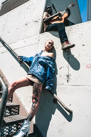 Woman Standing On Stairs Leaning On Wall And Man Playing The Guitar