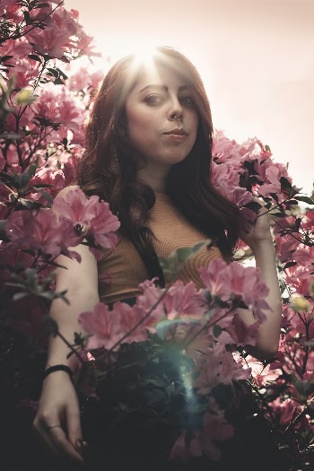Woman Standing Wearing Brown Cap-sleeved Top in Front of Pink Flowers