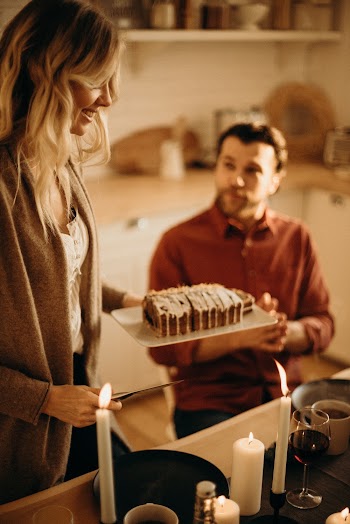 Woman Standing While Serving Sliced Cake and Man Sitting Near Table