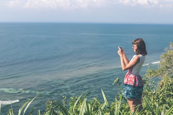 Woman Standing White and Blue Floral Dress Holding Smartphone in Grass Area