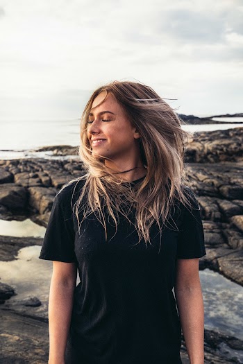 Woman Stands Near Body of Water and Wind Blows Her Hair