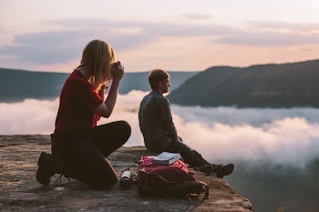 woman taking photo of man sitting on cliff at daytime