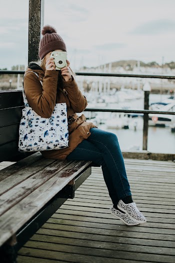 Woman Taking Picture While Sitting on Wooden Bench